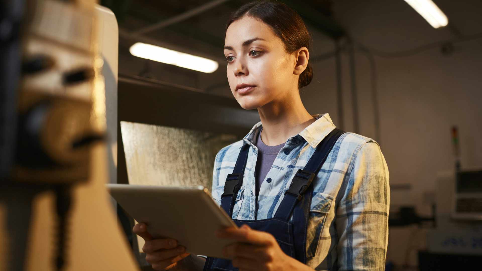 Female factory/plant worker in overalls using digital tablet in her work