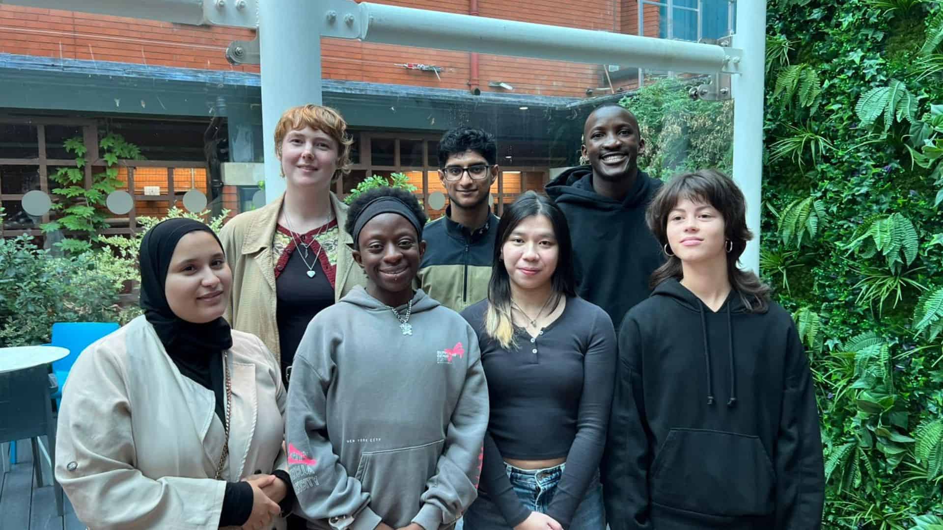 The Future Generations Panel (a diverse group of young people) stood together in front of a background of plants